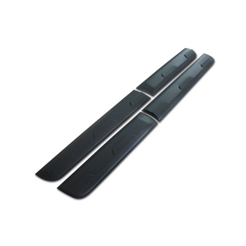 Two long, black plastic side skirts, designed for a vehicle, lie parallel on a plain white background. The skirts feature subtle ridges and edges for aerodynamics or aesthetics.