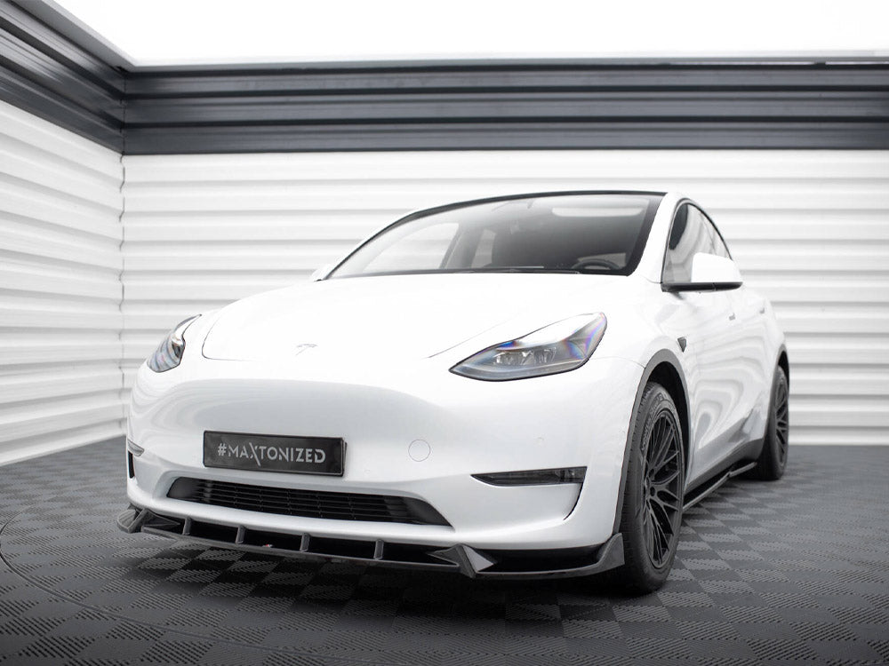 A white car with tinted windows and black wheels is parked in a light grey showroom. The license plate displays "#MAXTONIZED."