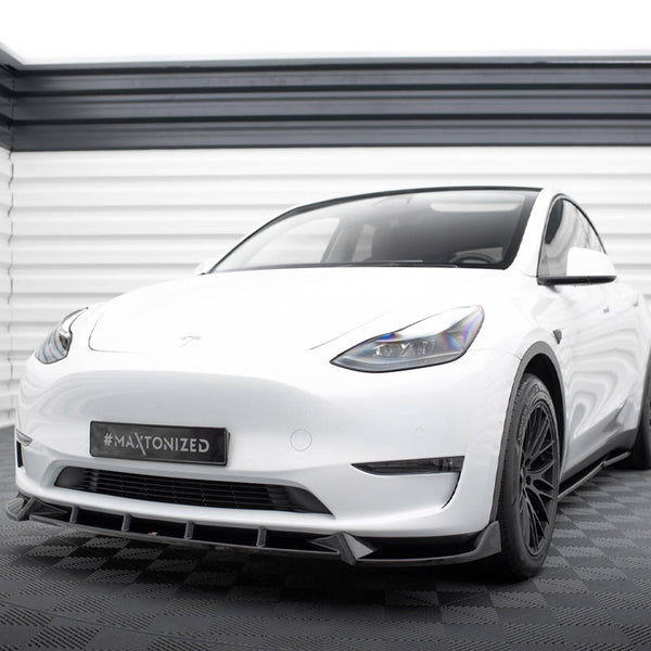 A white car with tinted windows and black wheels is parked in a light grey showroom. The license plate displays "#MAXTONIZED."