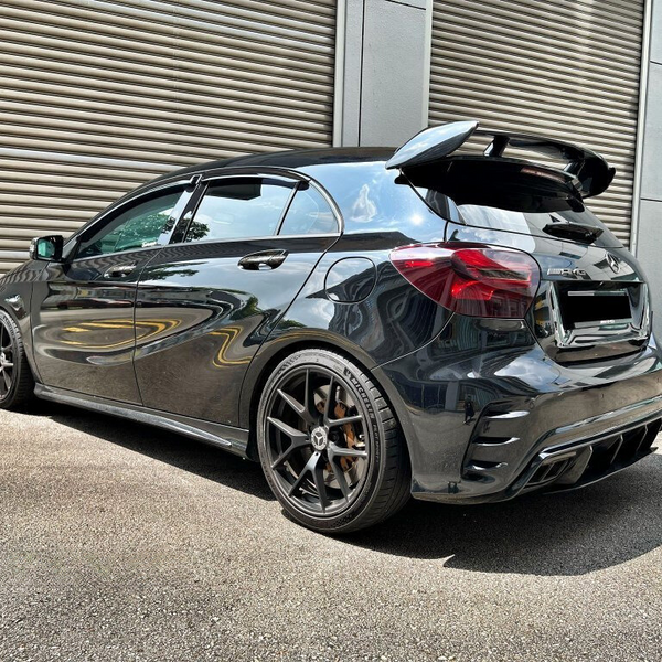 A sleek, black hatchback car, parked on a concrete surface, features sporty wheels and a prominent rear spoiler. It's positioned near a large industrial-style metal garage door.