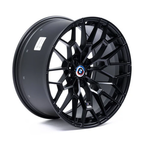 A sleek, black alloy wheel with an intricate, angular spoke design features a central emblem. It rests standing on a white background.