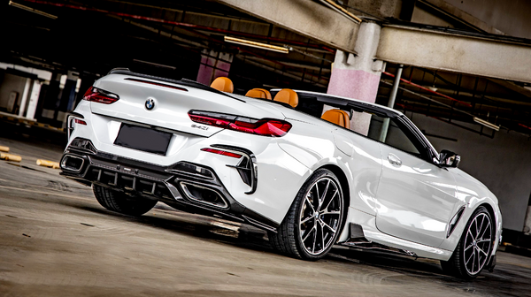 Convertible BMW car, parked, in a dimly lit concrete parking garage. The car is white with notable rear design details and black, sporty wheels. A "840i" badge is visible.