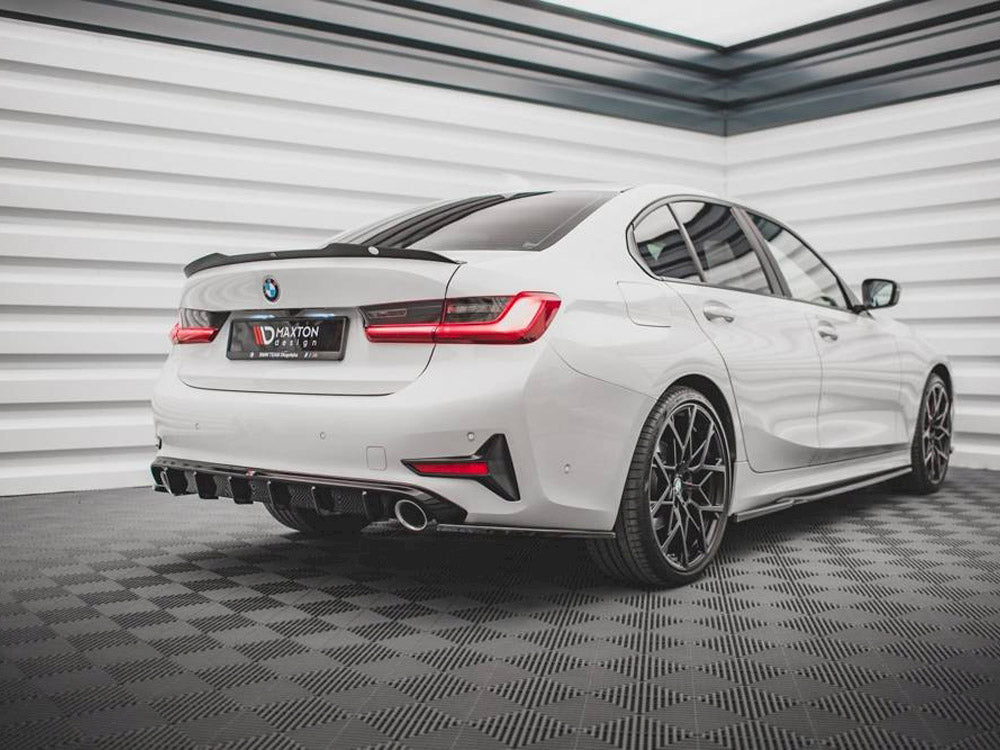 A white BMW sedan stands in a modern garage with a checkered floor. The rear features black diffuser accents and dual exhaust pipes. Text on the license plate reads "MAXTON DESIGN."