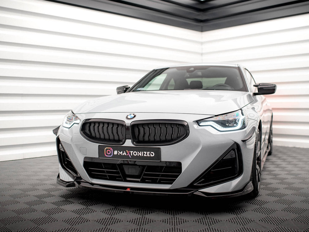 A gray BMW car is parked stationary in a modern showroom with white, geometric walls. The license plate displays Instagram text: "#MAXTONIZED".