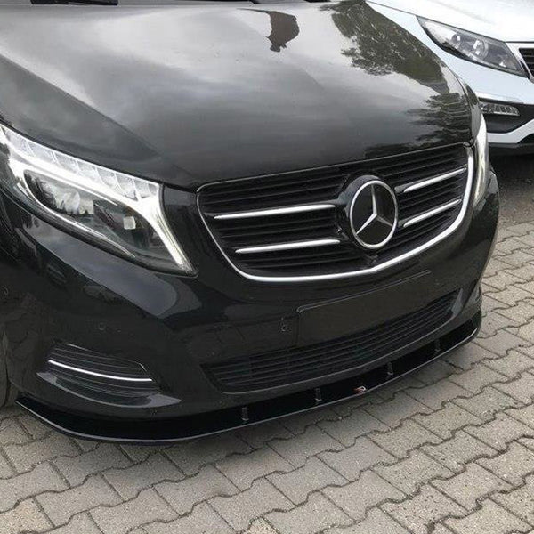 A black Mercedes-Benz vehicle is parked on a paved surface alongside a white Kia, in an outdoor setting. The Mercedes emblem is prominently displayed on the grille.