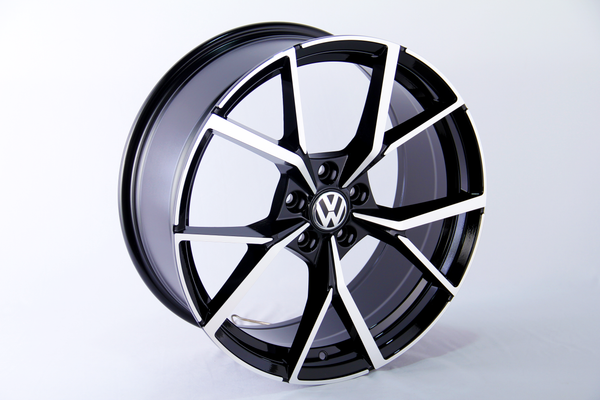 A sleek, black and silver alloy wheel with intricate spoke design and a central VW logo, standing against a plain white background.