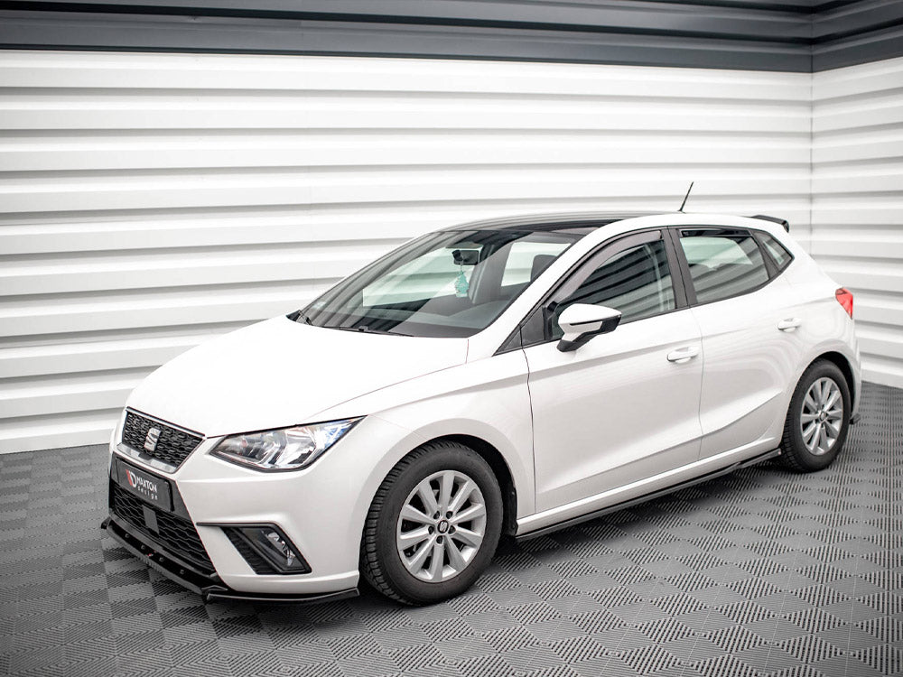 A white hatchback car is parked in a modern, well-lit showroom with patterned flooring and walls.