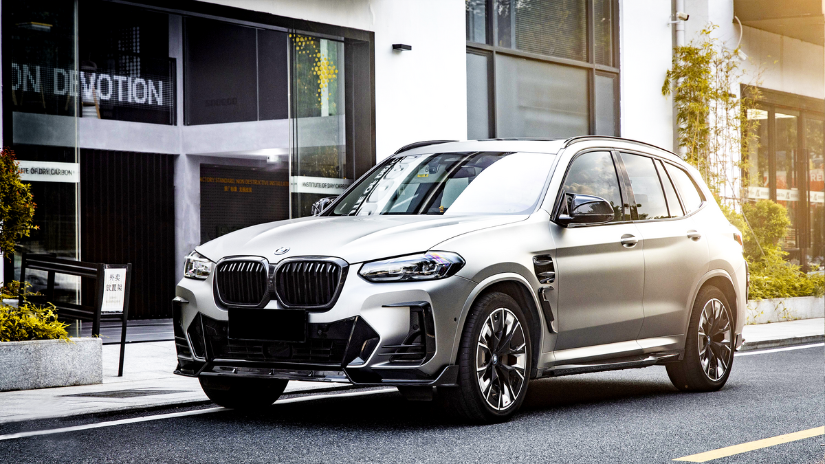 A silver SUV is parked on a city street beside a modern building with large windows. Text on the building reads "INSTITUTE OF DRY CARBON."
