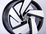 A car wheel rim with a sleek black and white design, featuring the Volkswagen logo in the center, displayed against a plain white background.