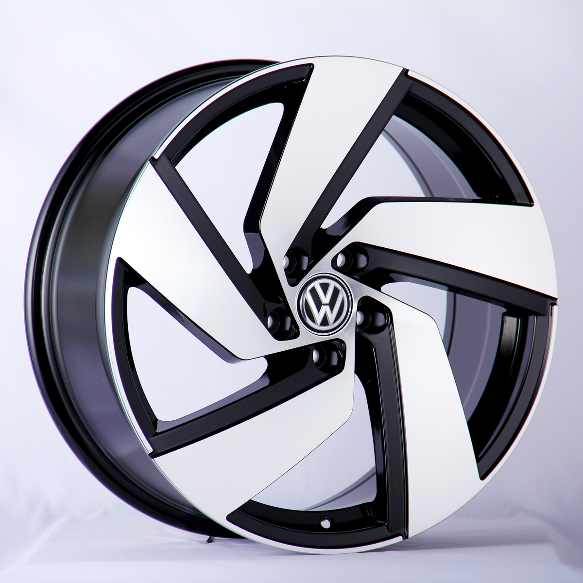 A car wheel rim with a sleek black and white design, featuring the Volkswagen logo in the center, displayed against a plain white background.