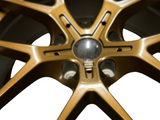 A bronze-colored alloy wheel with multiple spokes is positioned against a plain white background, emphasizing its intricate design and metallic finish.
