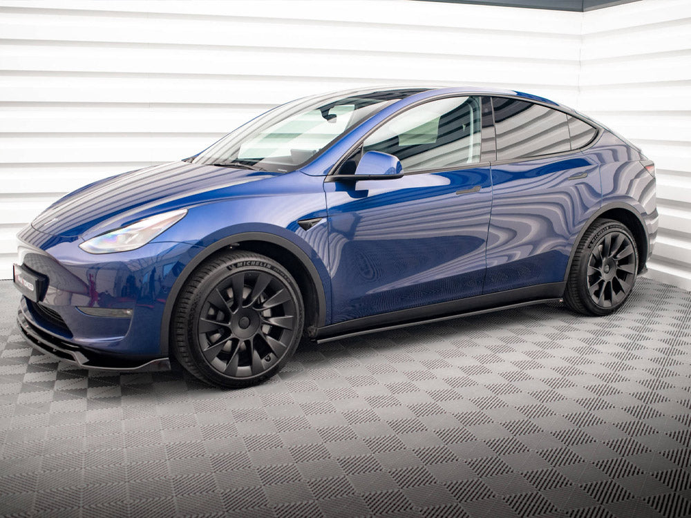 A blue car is parked in a brightly lit room with a checkered floor and white, striped walls. The vehicle features black wheels with "MICHELIN" on the tires.