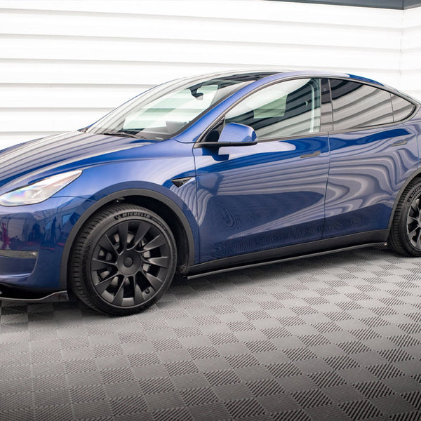 A blue car is parked in a brightly lit room with a checkered floor and white, striped walls. The vehicle features black wheels with "MICHELIN" on the tires.