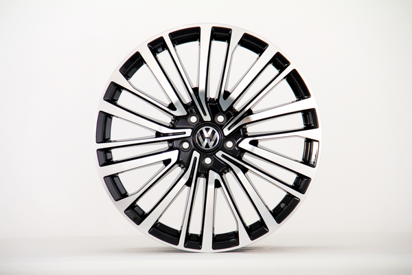 A shiny black and silver alloy wheel with a Volkswagen logo in the center is displayed against a plain white background.