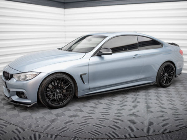 A sleek silver coupe car is parked in a corner of a patterned garage with textured flooring and paneled walls, featuring black wheels and tinted windows.