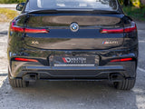 A black BMW X4 M40i is parked on a gravel surface. The license plate reads 