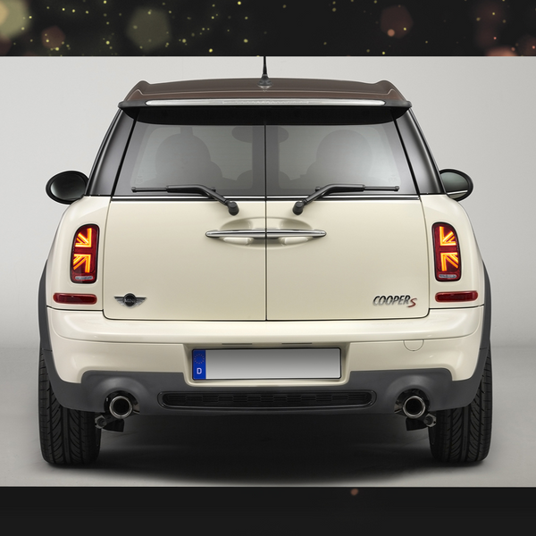 A cream-colored car, viewed from the rear, displays distinctive taillights and dual exhausts against a plain backdrop. The "Cooper S" badge and Mini emblem are visible.