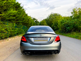 A silver Mercedes-Benz car is parked on a road, surrounded by lush green trees under a partly cloudy sky.
