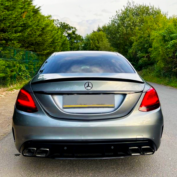 A silver Mercedes-Benz car is parked on a road, surrounded by lush green trees under a partly cloudy sky.