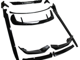Black automotive body kit parts laid out on a white surface; several pieces include spoilers, skirts, and bumpers, all designed for vehicle modification.