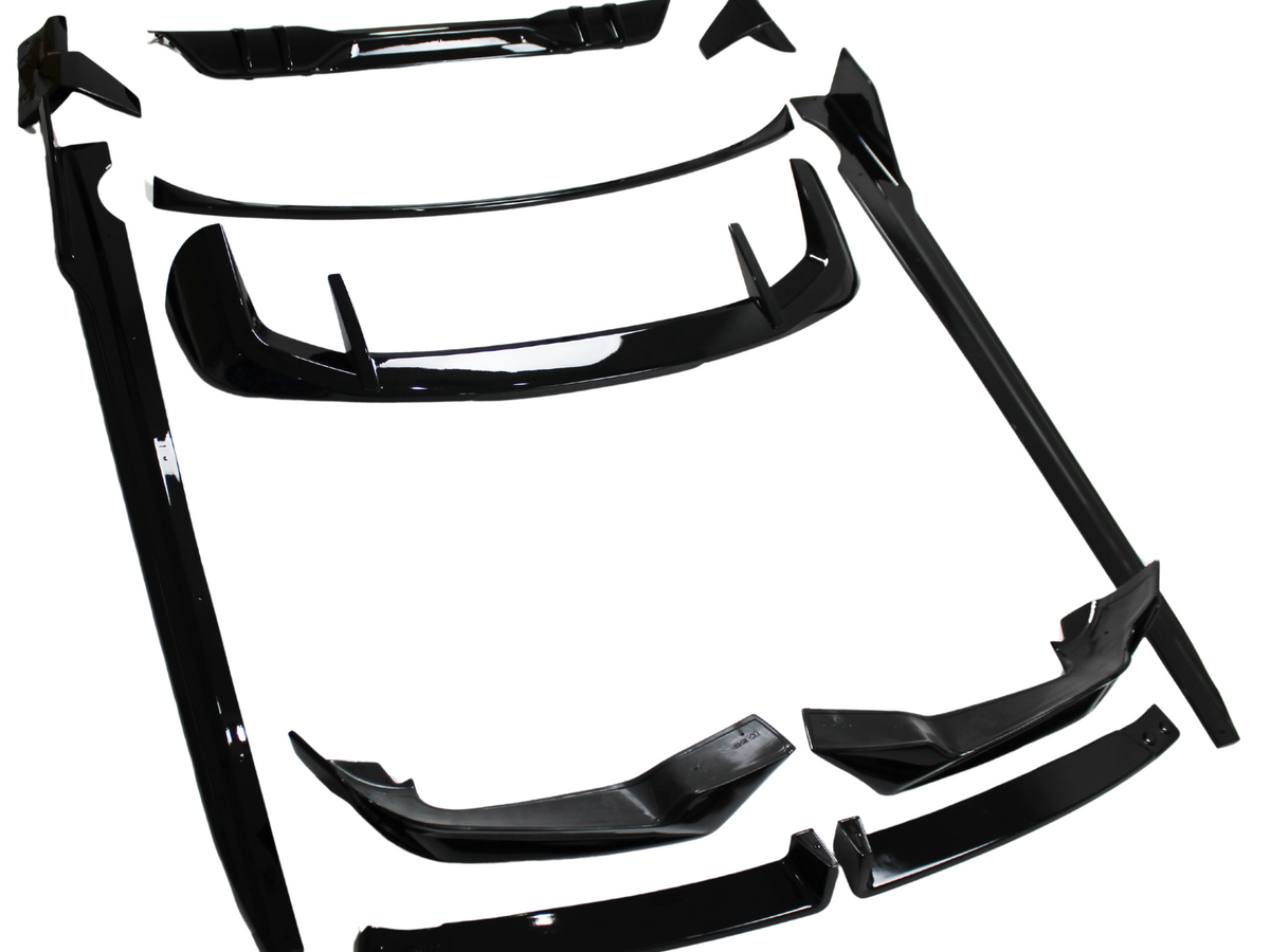 Black automotive body kit parts laid out on a white surface; several pieces include spoilers, skirts, and bumpers, all designed for vehicle modification.