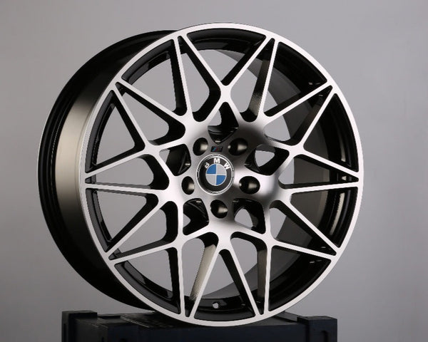 A BMW wheel with intricate multi-spoke design rests atop a dark-blue crate, featuring a faint Union Jack pattern and partial text "GA" visible, against a plain grey background.