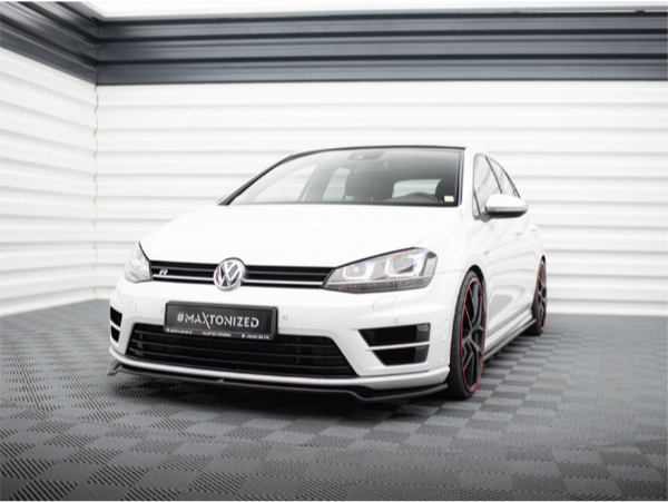 A white Volkswagen car is parked in a showroom with patterned flooring and white walls. Text on the license plate reads "#MAXTONIZED MAEXTON-DESIGN.COM." The setting is bright and modern.
