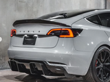 A gray Tesla car is parked indoors, featuring illuminated tail lights and a sleek design. The letters 