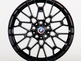 A glossy black alloy wheel with intricate geometric design, displaying the BMW emblem at its center. It is standing upright against a plain white background.