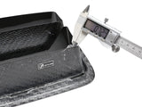 A digital caliper measures the thickness of a black, textured carbon fiber part, displaying 
