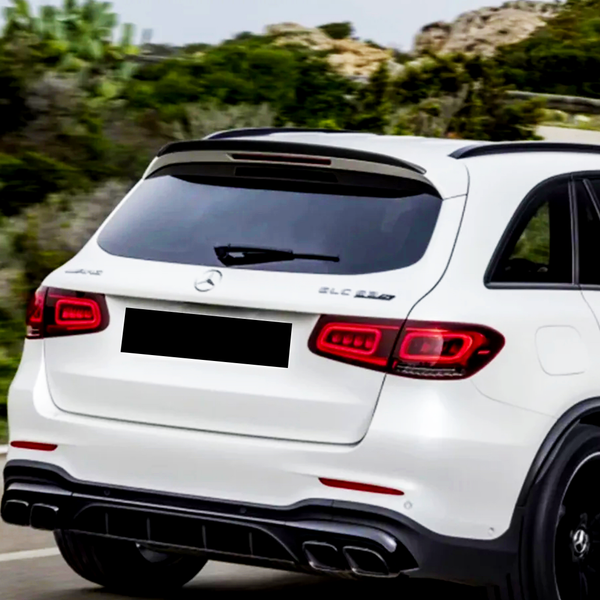 A white SUV drives on a road with surrounding greenery. Text on the vehicle reads "GLC 63S" and "AMG" near the Mercedes logo.