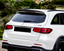 A white SUV drives on a road with surrounding greenery. Text on the vehicle reads "GLC 63S" and "AMG" near the Mercedes logo.
