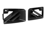 Two black carbon fiber car vents, featuring angular fins, rest on a plain white background, highlighting their sleek design and glossy surface.