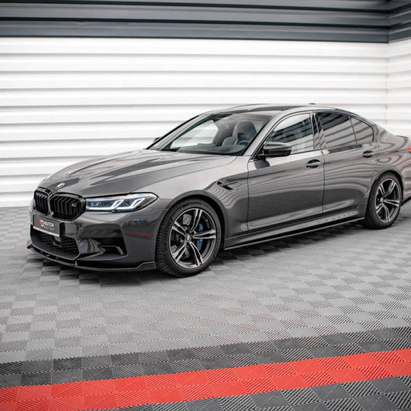 A sleek, gray sedan is parked on a patterned floor in a modern showroom with striped walls. The license plate reads "VATTEN EXKLUSIVE."