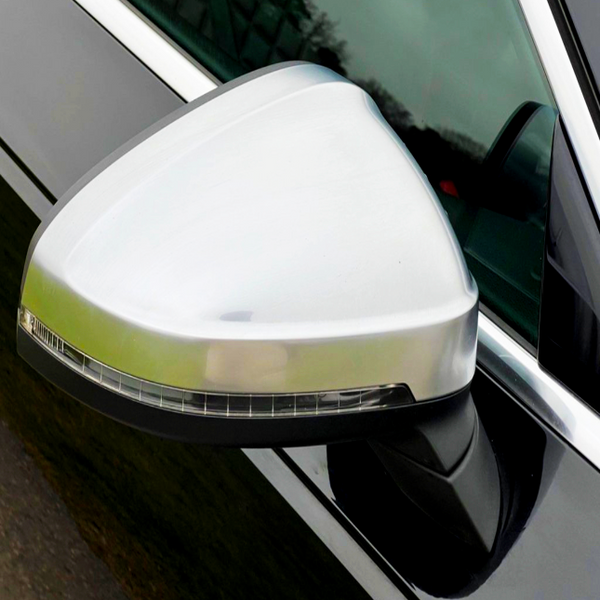 A silver car side mirror features an integrated turn signal, attached to a black vehicle door in daylight.