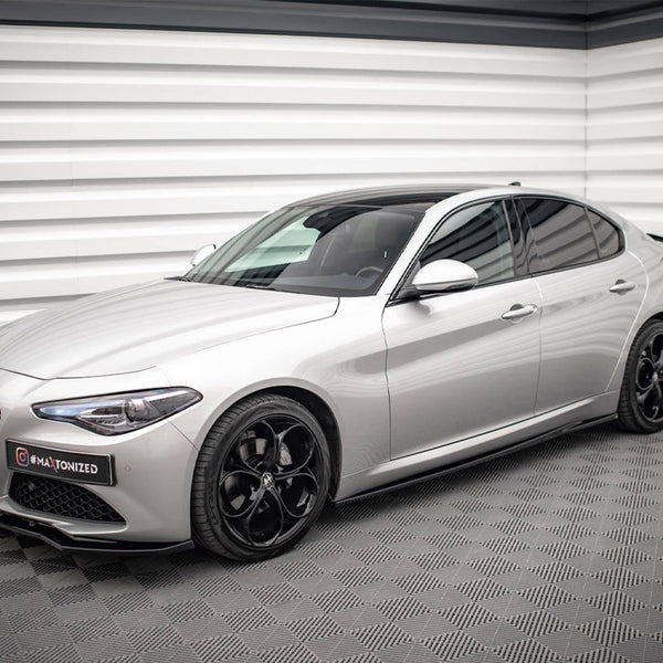 A sleek silver sedan is parked in a modern showroom with textured white walls and a patterned floor. A sign on the front reads "#MAXTONIZED".