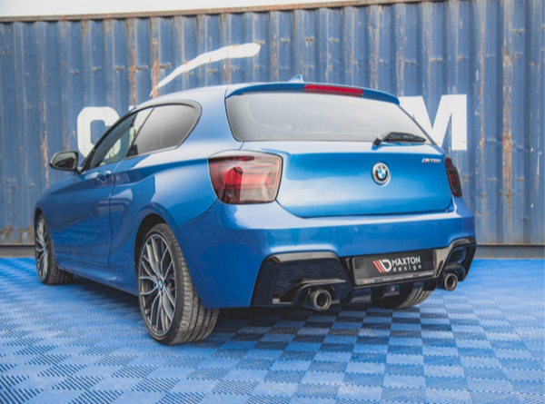 A blue BMW hatchback is parked on a checkered blue surface, near a blue shipping container. The license plate reads "MAXTON DESIGN."