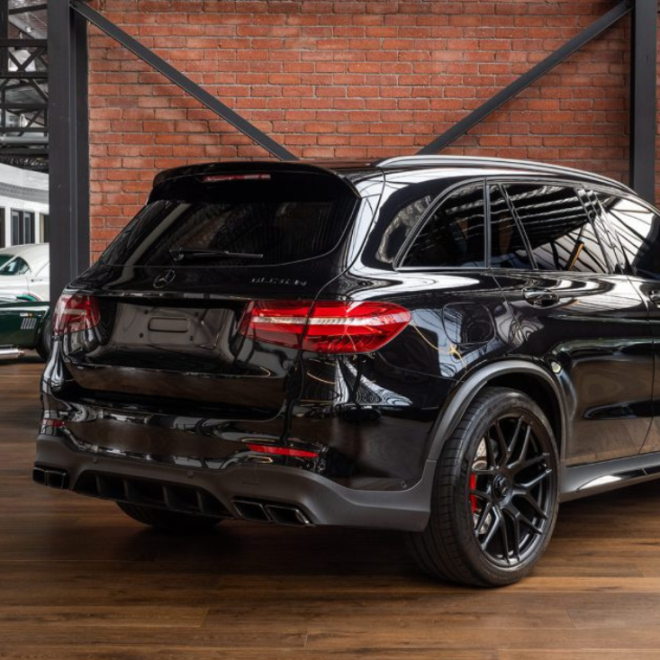A black SUV with tinted windows is parked on a wooden floor inside a brick-walled showroom, featuring a high, industrial-style ceiling.