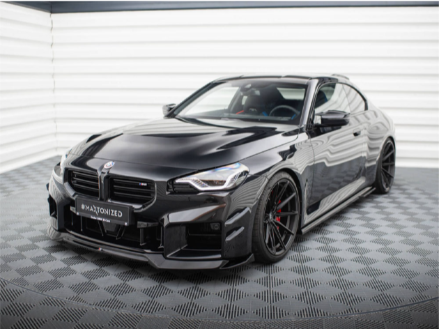 A sleek black sports car is parked on a checkered floor, with the text "#MAXTONIZED" on the front plate, set against a white, ridged background.