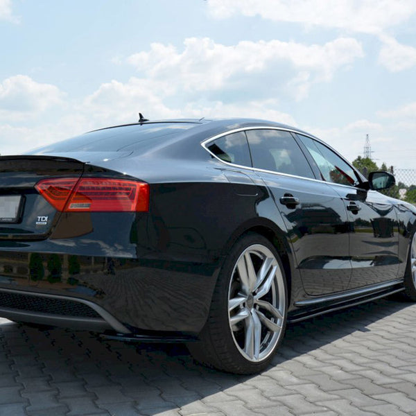 A black Audi A5 parked on a paved area under a partly cloudy sky. The car's sleek design and silver alloy wheels are prominent. Text includes "A5" and "TDI."