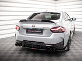 A silver BMW M240i is parked in a white, geometric-patterned room, featuring quad exhausts and elegant taillights. The license plate reads 