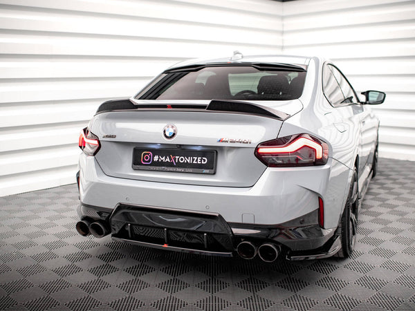 A silver BMW M240i is parked in a white, geometric-patterned room, featuring quad exhausts and elegant taillights. The license plate reads "#MAXTONIZED" with additional text: "Official Premium Partner MAZ 2021."