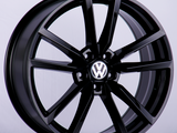 A glossy black alloy wheel is displayed upright with a visible silver Volkswagen logo at the center, set against a plain light gray backdrop.