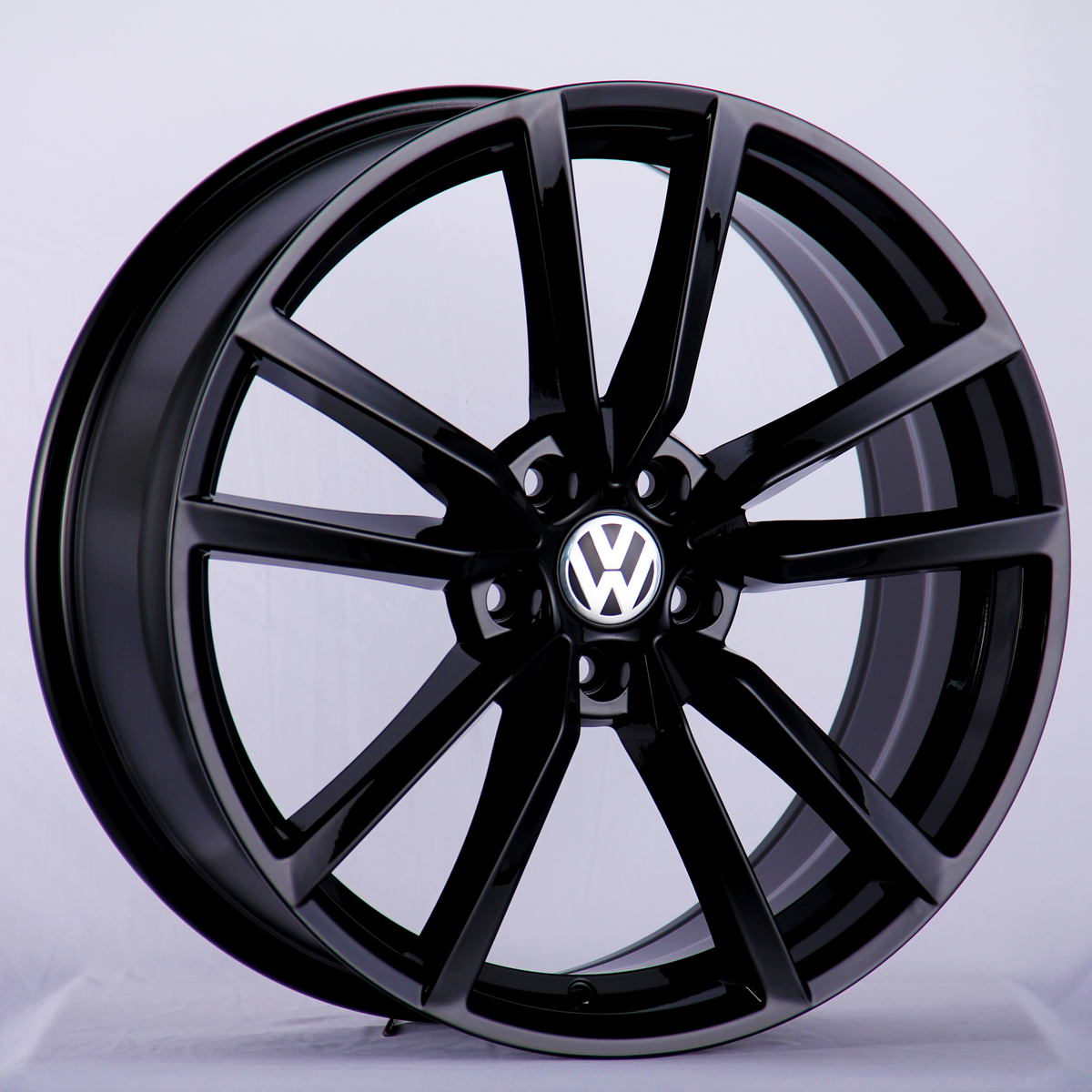 A glossy black alloy wheel is displayed upright with a visible silver Volkswagen logo at the center, set against a plain light gray backdrop.
