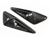 Two carbon fiber, triangular car accessories with polished surfaces and circular cutouts are placed on a plain white background.