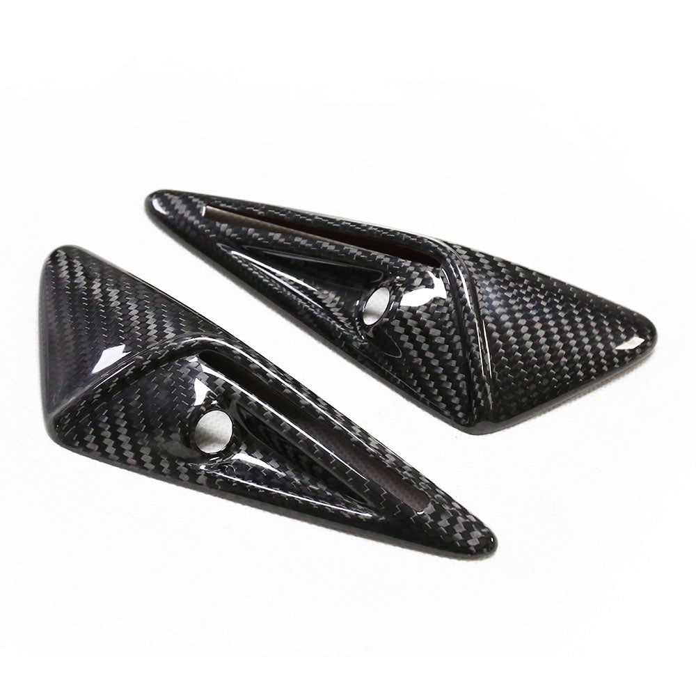Two carbon fiber, triangular car accessories with polished surfaces and circular cutouts are placed on a plain white background.