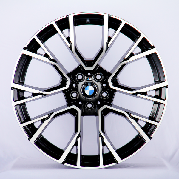 A black and silver alloy wheel features intricate spoke design with a BMW logo at the center, resting against a plain white backdrop.