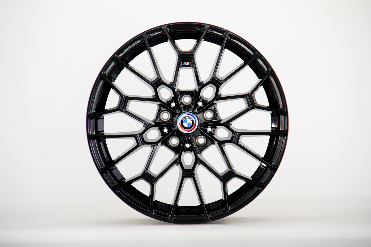 A black alloy car wheel features intricate spoke design, resting stationary, with a BMW logo in the center, set against a plain white background.