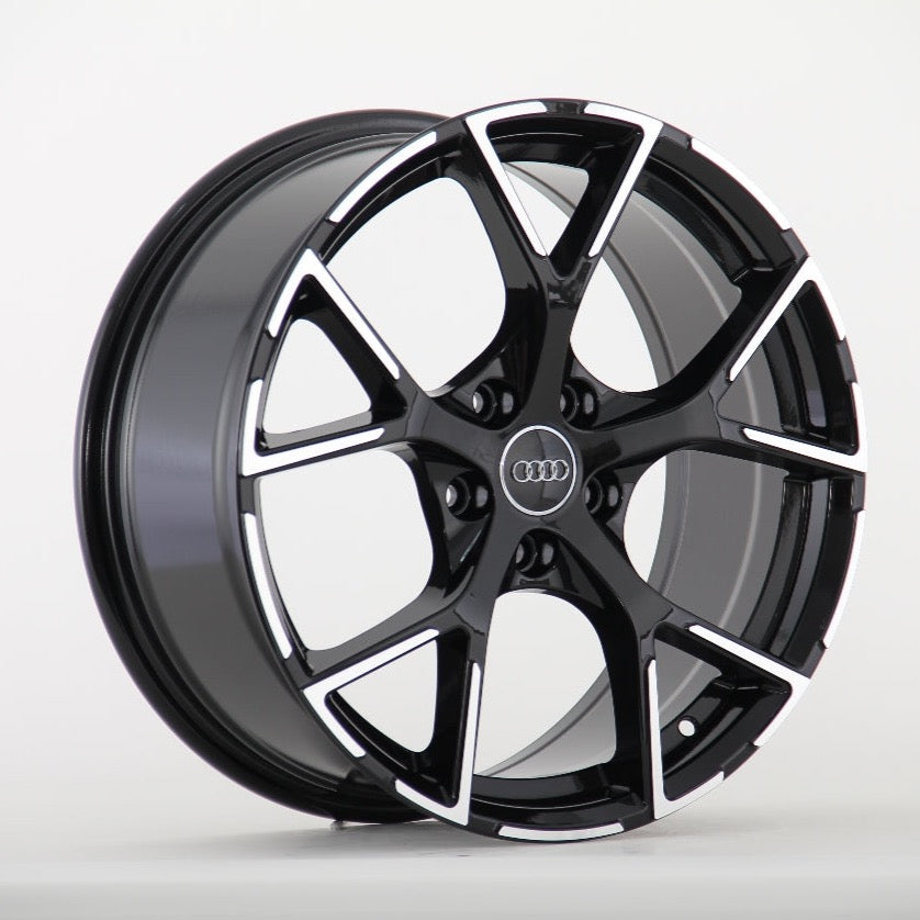 A black and silver alloy wheel with a five-spoke design, prominently featuring the Audi logo in the center, is displayed against a plain white background.