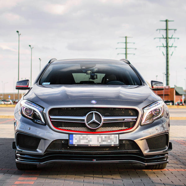 A silver Mercedes-Benz car is parked on a paved area. The setting is an open parking lot with utility poles and a cloudy sky in the background.